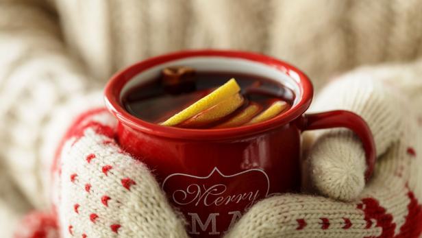 Hände in Fäustlingen halten eine volle Tasse Glühwein.