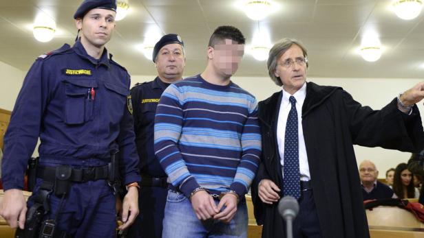 Ein Mann mit Handschellen wird von Justizwachebeamten und einem Anwalt umgeben.