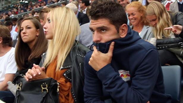 Zuschauer sitzen auf einer Tribüne, ein Mann mit Red Bull-Jacke verdeckt sein Gesicht.