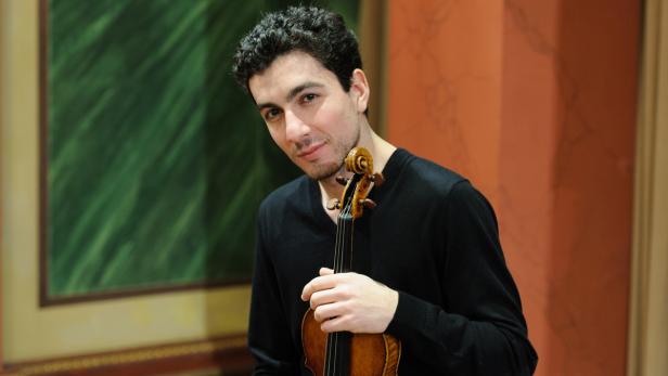 Ein junger Mann hält eine Geige in seinen Händen.