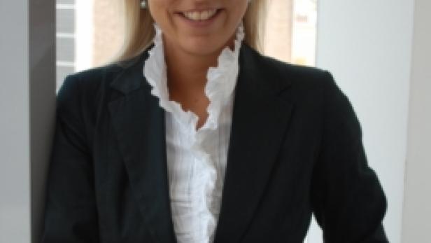 Eine blonde Frau in Blazer und Bluse lächelt in die Kamera.