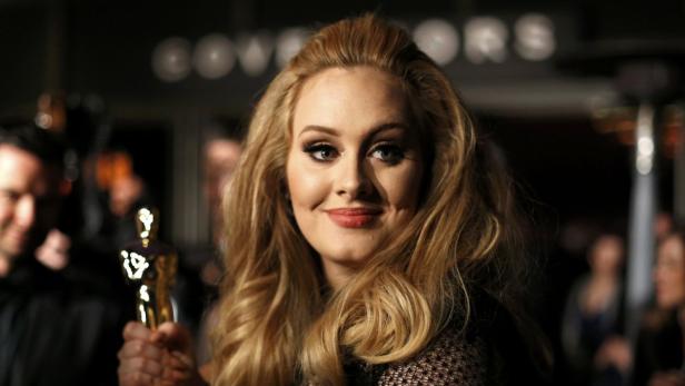 Adele hält eine Oscar-Statue in der Hand und lächelt.