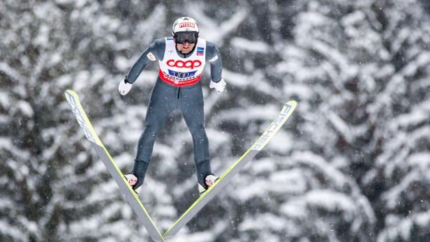 Ein Skispringer in der Luft vor einem verschneiten Hintergrund.