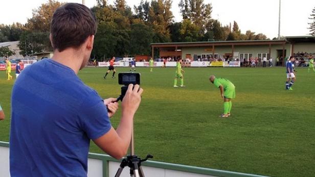 Ein Mann filmt mit seinem Smartphone auf einem Stativ ein Fußballspiel.