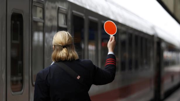 Eine Zugbegleiterin der Deutschen Bahn gibt mit einer roten Kelle ein Signal.