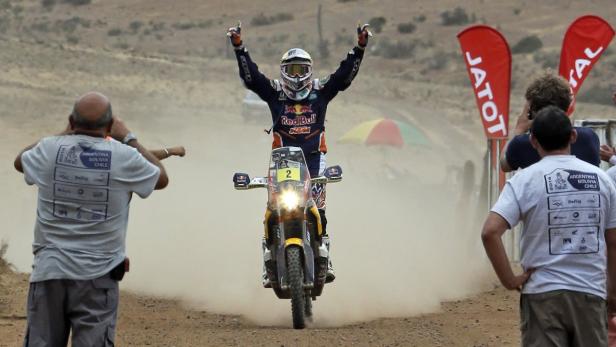 Ein Motorradrennfahrer jubelt mit erhobenen Armen nach dem Zieleinlauf der Rallye Dakar.