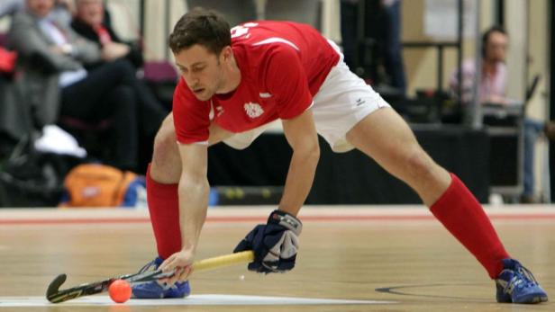 Ein Hockeyspieler in roter Sportkleidung ist bereit, den Ball zu schlagen.