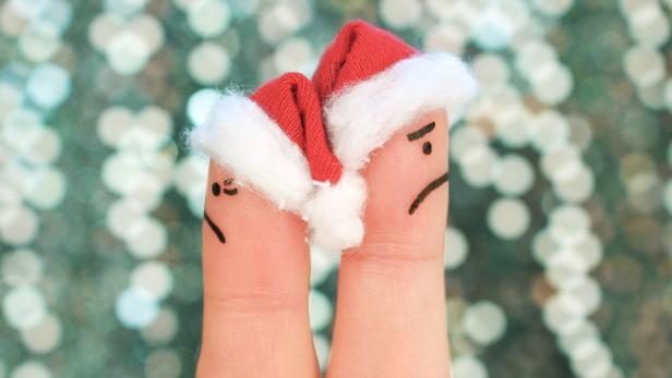 Symbolbild Tipps für die Feiertage: Zwei Finger mit roten Weihnachtsmützen, die sich voneinander abwenden
