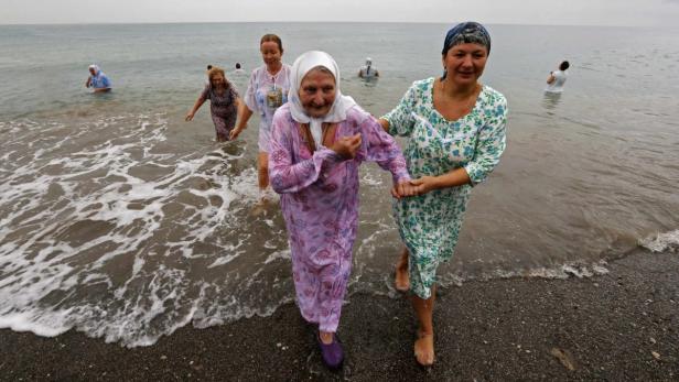Frauen in Kleidern steigen ins Meer, einige tragen Kopftücher.