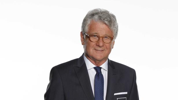 Ein Mann mit grauen Haaren, Anzug und Brille lächelt in die Kamera.