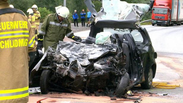 Ein völlig zerstörtes Auto nach einem Unfall, mit Feuerwehrleuten vor Ort.