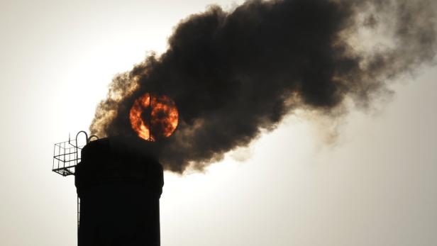 Schwarzer Rauch steigt aus einem Schornstein auf und verdeckt die Sonne.
