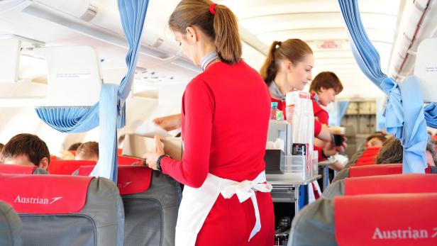 Flugbegleiterinnen servieren Getränke und Speisen in einem Flugzeug von Austrian Airlines.