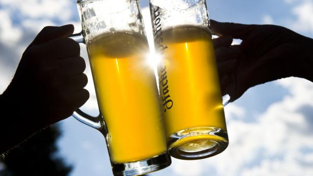 Zwei Bierkrüge der Marke Hacker-Pschorr werden vor blauem Himmel angestoßen.