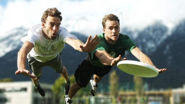 Zwei Männer hechten auf einer Wiese nach einer Frisbee.