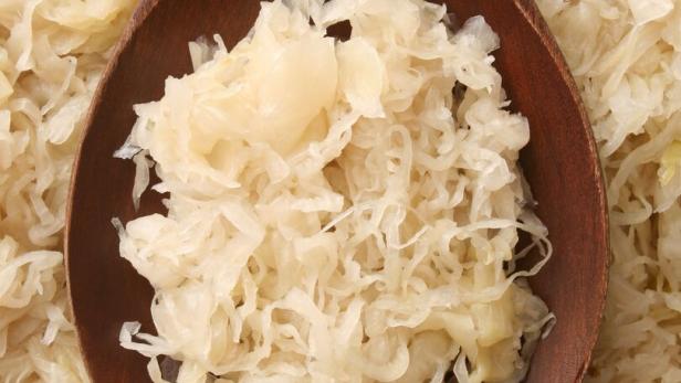Sauerkraut auf einem Holzlöffel, umgeben von weiterem Sauerkraut.