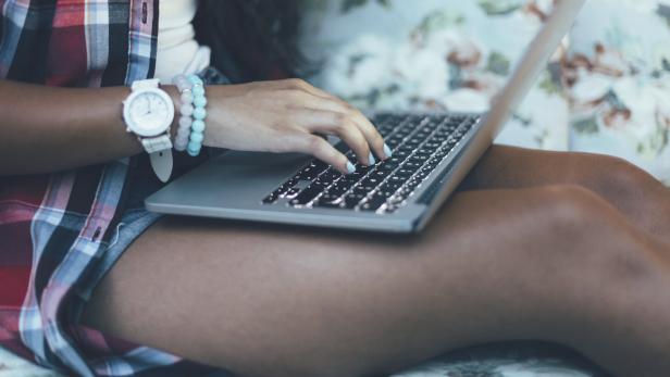 Eine Jugendliche sitzt mit einem Laptop auf dem Bett.