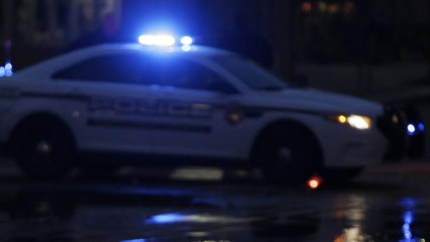 Ein Polizeiauto steht nachts mit eingeschaltetem Blaulicht auf einer nassen Straße.
