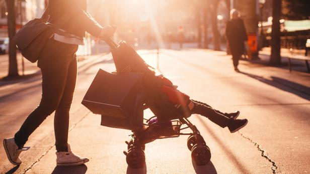 Eine Person schiebt einen Kinderwagen mit Einkaufstaschen bei strahlendem Sonnenschein.