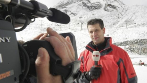 Ein n-tv Reporter steht mit Mikrofon vor einer verschneiten Berglandschaft.