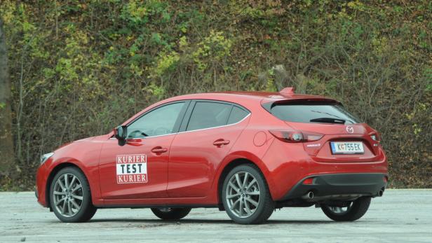 Ein roter Mazda 3 parkt vor einer grünen Hecke.