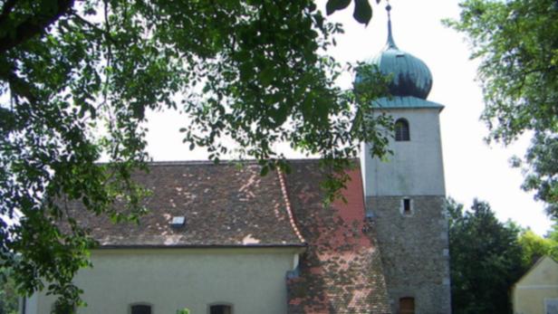 Eine Kirche mit einem Turm und einem grünen Kuppeldach, teilweise von Bäumen verdeckt.