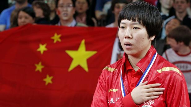 Die chinesische Tischtennisspielerin Ding Ning mit der Hand auf der Brust vor der chinesischen Flagge.