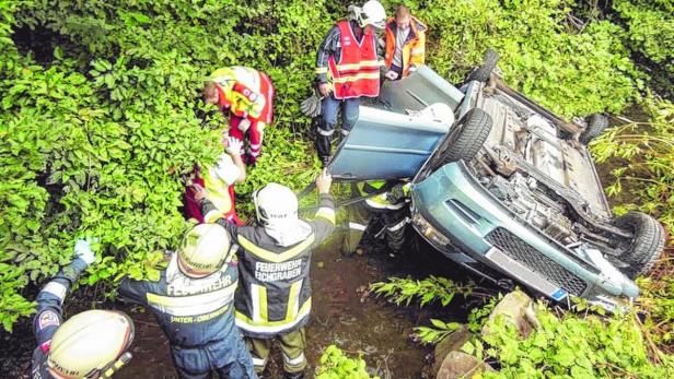 Ein auf dem Dach liegendes Auto wird von Rettungskräften geborgen.
