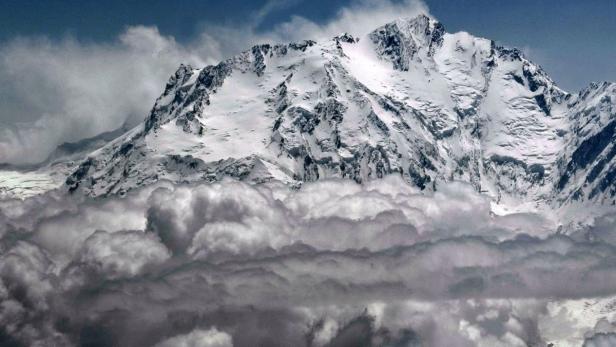 Ein schneebedeckter Berggipfel ragt über eine Wolkendecke hinaus.