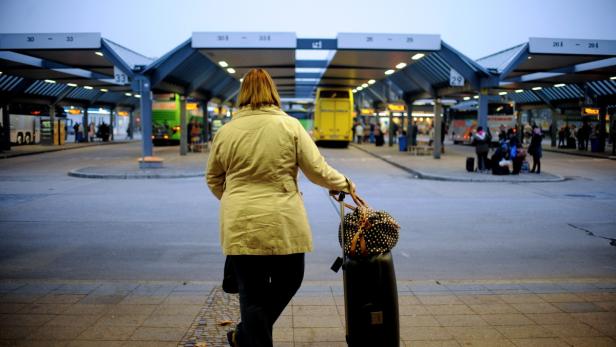 Eine Frau mit Koffer betritt einen Busbahnhof.