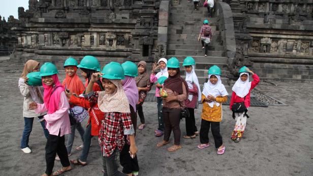 Eine Gruppe junger Frauen mit Kopftüchern und Bauhelmen vor einem Tempelgebäude.