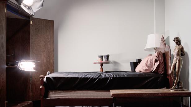 Ein Schlafzimmer mit einem Bett, einem Schrank, einer Statue und Beleuchtung für ein Fotoshooting.