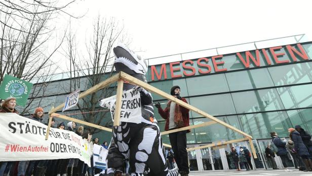 Demonstranten, darunter eine Person im Dinosaurierkostüm, protestieren vor der Messe Wien.