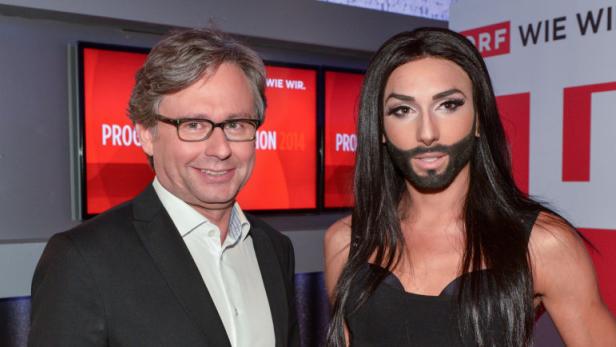 Ein Mann mit Brille und Anzug steht neben Conchita Wurst.