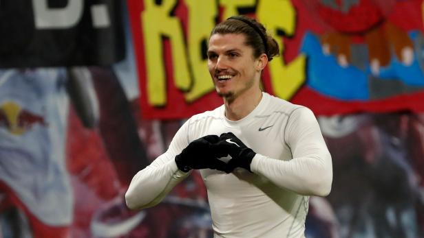 Ein lächelnder Fußballspieler mit Handschuhen formt ein Herz mit seinen Händen.