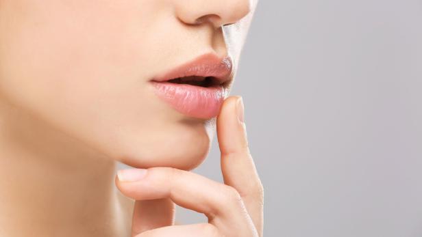 Eine Frau berührt mit einem Finger ihre Lippen.