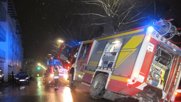 Ein Feuerwehreinsatz in einer dunklen, nassen Straße mit mehreren Einsatzfahrzeugen.