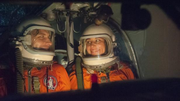 Zwei Astronauten in orangefarbenen Anzügen und Helmen sitzen in einem Raumschiff.