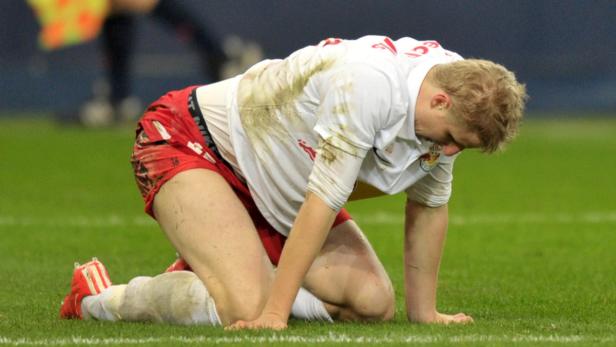 Ein Fußballspieler kniet erschöpft und schmutzig auf dem Rasen.