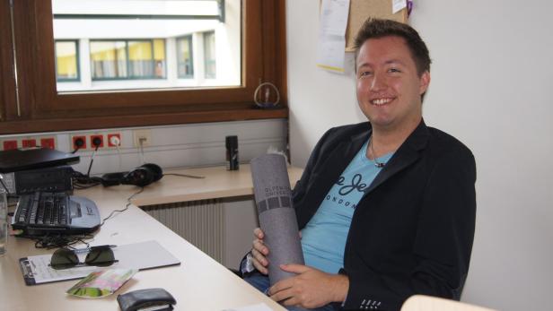 Ein Mann sitzt an einem Schreibtisch und hält eine Urkunde der Alpen-Adria-Universität.