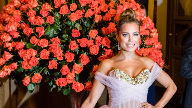 Eine Frau in einem rosa Kleid vor einem großen Rosenarrangement beim 15. Semperopernball in Dresden.