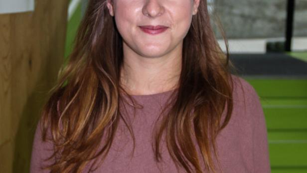 Eine junge Frau mit langen braunen Haaren und einem rosa Pullover lächelt in die Kamera.