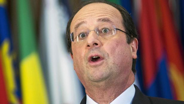 François Hollande mit überraschtem Gesichtsausdruck vor einem Hintergrund mit Flaggen.