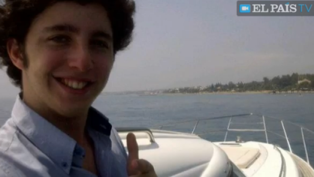 Ein junger Mann lächelt auf einer Yacht vor einer Küstenlinie.
