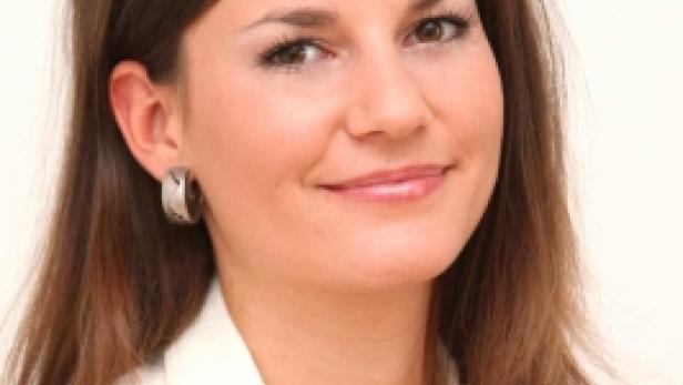 Eine lächelnde Frau mit braunen Haaren und weißer Bluse blickt in die Kamera.