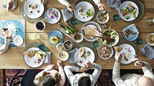 Eine Gruppe von Menschen isst gemeinsam an einem Tisch mit verschiedenen Speisen wie Hummus und Salat.