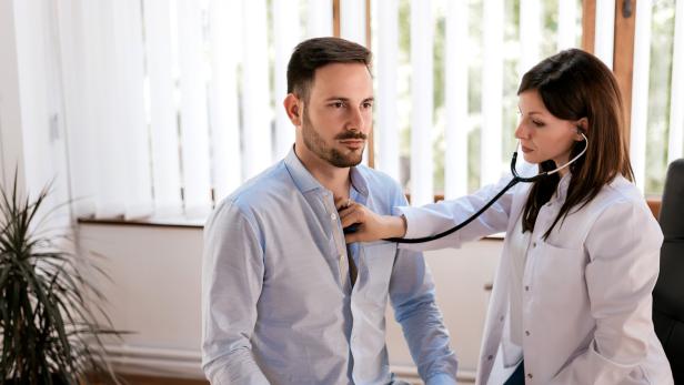Eine Ärztin untersucht einen Patienten mit einem Stethoskop im Behandlungszimmer.
