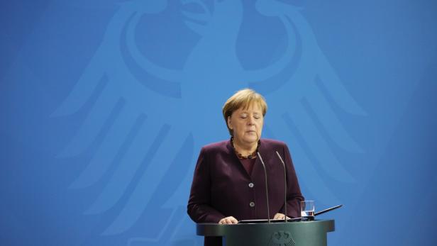 Angela Merkel steht vor einem blauen Hintergrund mit dem Bundesadler.