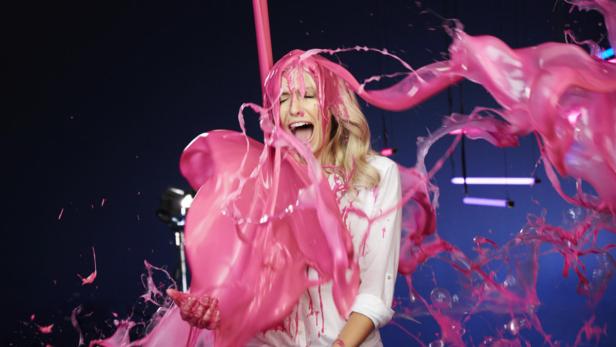 Eine Frau wird mit rosa Farbe übergossen und schreit.