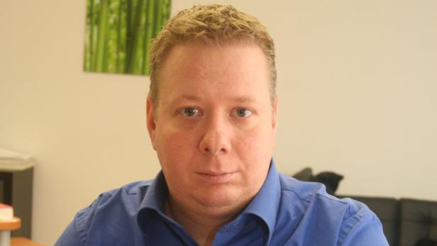 Ein Mann mit blonden Haaren und blauem Hemd blickt in die Kamera.